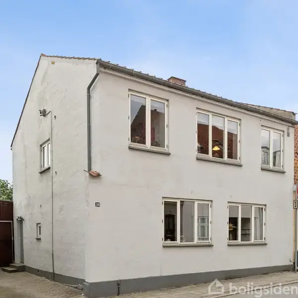 Toetagers hvidt hus står på en gade med en tilhørende garage og gavl. Ved siden af ses et cremefarvet hus med tegltag. Opaf huset er et færdselsmærke med parkeringsforbud.