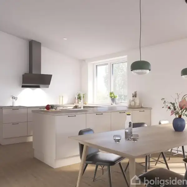 Et moderne køkken med en lys træbordplade og hvide skabe. På bordet står en blå vase med blomster. Rummet er lyst med store vinduer og hængelamper.