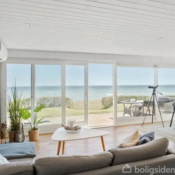 Et bord står udendørs med en bakke fuld af lys og sten ved siden af to krus og en lille dansk flag. I baggrunden ses græs og en udsigt over havet.