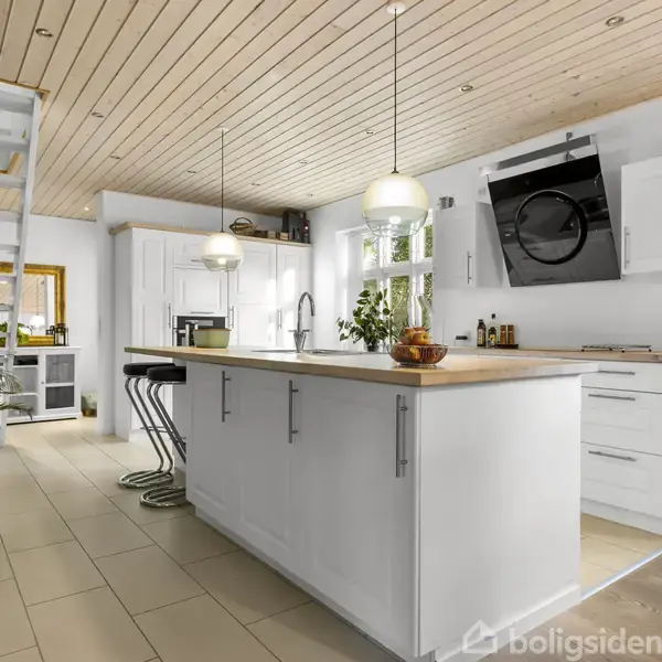 Et moderne køkken med en stor hvid ø som det centrale objekt. Øens overflade har en træfinish, og der hænger lamper over den. Flere siddepladser og grønne planter findes i rummet.