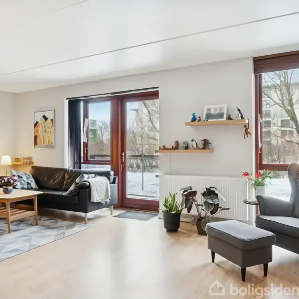 En stue med en sort sofa og lænestol, placering ved glasdøre mod en sneklædt have. Lys træparketgulv, planter og hylder med dekorationer skaber en hyggelig atmosfære.