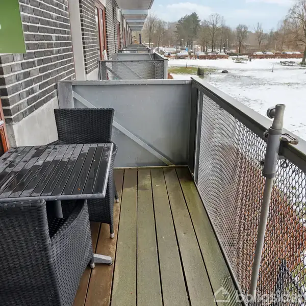 Altan med to sorte fletstole og et bord står stille. Ved siden af er et skilt med teksten "TIL SALG". I baggrunden ses et snedækket landskab.