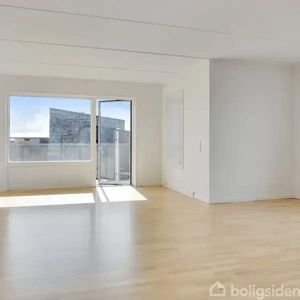 Et lyst rum med trægulv og store vinduer. Dør åbner til balkon med udsigt over bybygning. Hvidmalede vægge skaber en minimalistisk atmosfære.