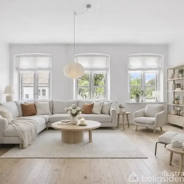 En lys stue indeholder en stor, beige sofa med puder, omgivet af lænestole og et rundt sofabord. Store vinduer lukker naturligt lys ind, mens planter og reoler skaber en hyggelig atmosfære.