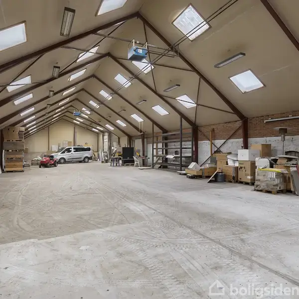 Et stort lagerlokale med højt til loftet. Biler står parkeret til venstre, mens kasser og materialer er stablet til højre. Loftsvinduer og lamper lyser rummet op.
