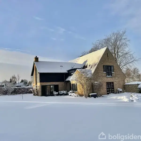 En gulstensvilla med rødt tegltag står foran en grusbelagt indkørsel og grønne buske. Omkring huset er der træer og en blå himmel. Tekst: "VISUALISERING AF NYT TAG".
