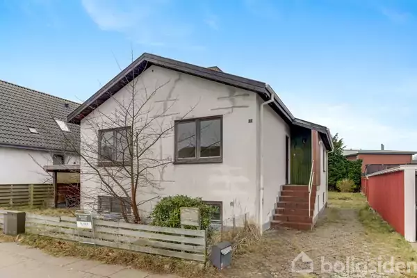 Huset står stille i et villakvarter, omgivet af græs og en lille hæk. Fronttrappen fører til hoveddøren, mens en postkasse er placeret ved indgangen.
