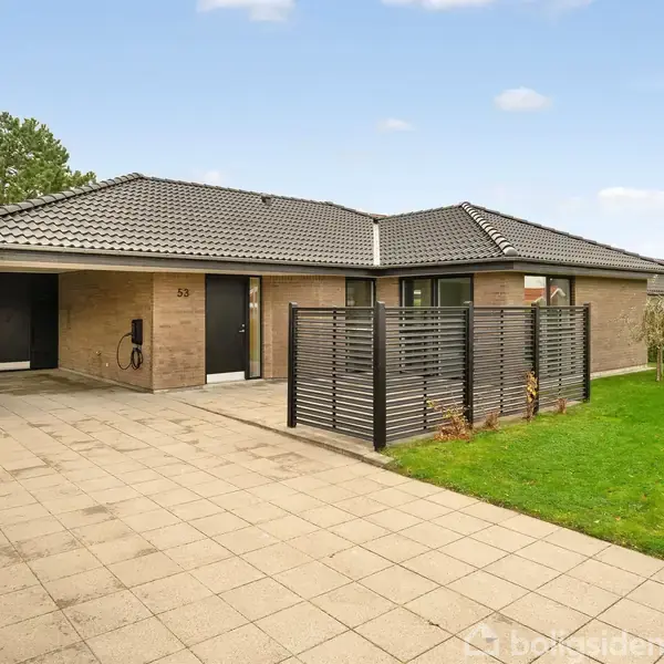 En moderne murstensvilla med mørkt tag står stille ved en flisebelagt indkørsel og en velplejet græsplæne. Nummer "33" er synligt ved hoveddøren.