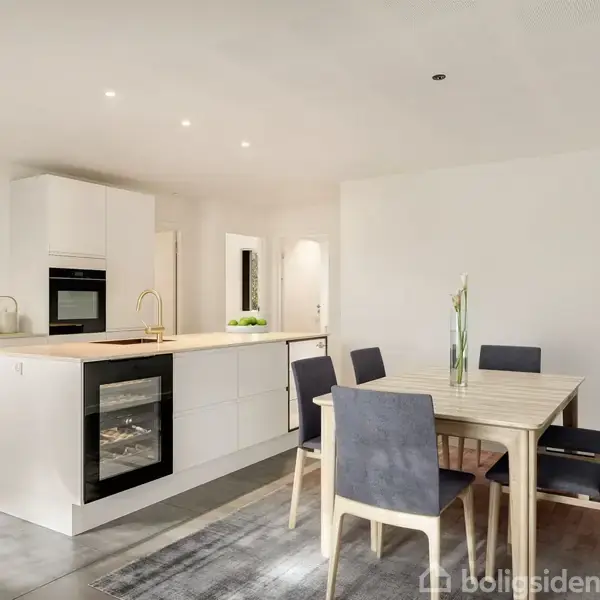 Køkken med hvide skabe og indbygget ovn, køkkenø med kogeplade, og spisebord med seks mørke stole. Lyst og moderne rum med minimalistisk indretning.