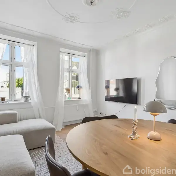 En moderne stue med hvid sofa (objekt), placeret i en lys stue med to store vinduer, fjernsyn på væggen, rundt spisebord med lampe og stearinlys (kontekst).