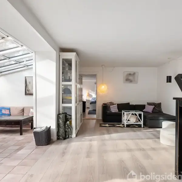 Stue med sort sofa og spisebord. Sofaen står til højre foran en væg og brændeovn, mens spisebordet står til venstre i en lys vinterstue med glasparti.