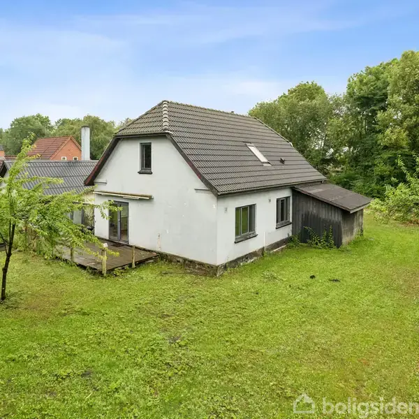 Et hvidt hus med gråt tag står stille på en grøn græsplæne omgivet af træer og buske i et villakvarter. Indskrevet tekst: "boligsiden".