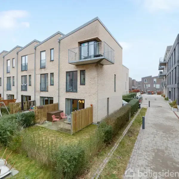 Rækkehuse i moderne stil står på række. En lille have med hegn og terrasse ses foran hvert hus. En stenbelagt sti løber langs husene gennem boligområdet.