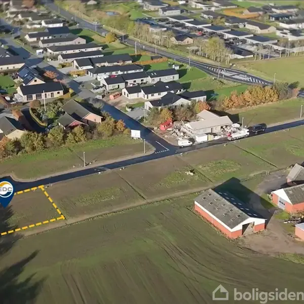 Parcellen er markeret med et EDC-skilt omgivet af en gul stiplet linje. Det ligger ved en vej i et beboelsesområde med mange huse og grønne områder.