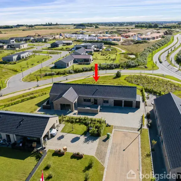 Et hus står i et boligområde med flere lignende huse omkring. En rød pil peger mod huset, der har en gårdsplads foran, omgivet af grønne områder og veje i nærheden.