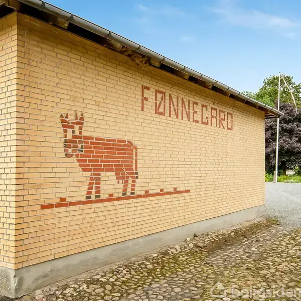 Bygning af gul mursten med murstenskunst, der forestiller en ko og teksten "Fønnegård". Tallet "29" ses på muren. Omkring bygningen er der en indkørsel og grønt landskab.
