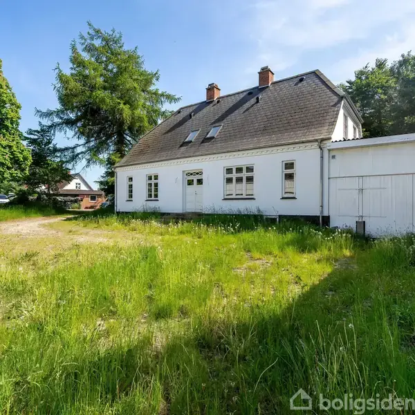 Trappe fører opad, flisegulv dominerer, en åben dør viser et badeværelse med spejl og vask. Skab hænger over døren. Lysegrå vægge i moderne rum.