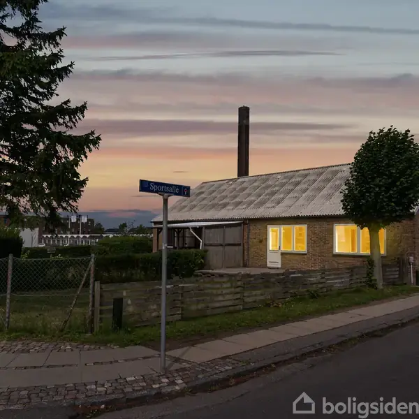 Et hus med lysende vinduer står ved en vej under en skumringshimmel. En vejskilt med teksten "Sporea" ses ved et hegn ved fortovet.