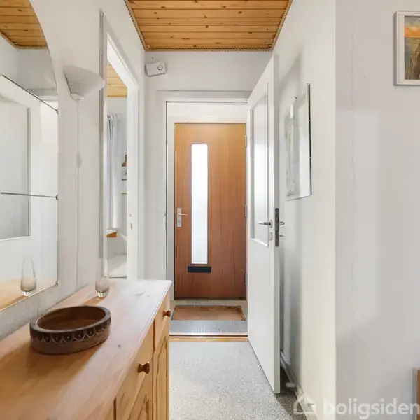 En gang med en træskænk og spejl på venstre side; en åben dør fører til en lysindfaldende hovedindgang. Vægge har kunstværker. Træloft giver en hyggelig atmosfære.