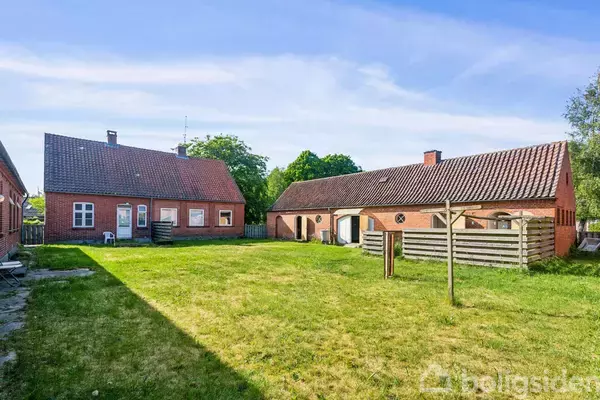 To murstenshuse med røde tage står over for hinanden i en græsklædt gårdhave med et tøjstativ imellem dem. Der er træer i baggrunden under en blå himmel.