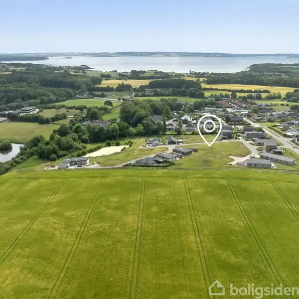 Landsby set fra luften med marker i forgrunden. Et ikon markerer en bestemt bygning i bebyggelsen. Der er skov og en stor sø i baggrunden.