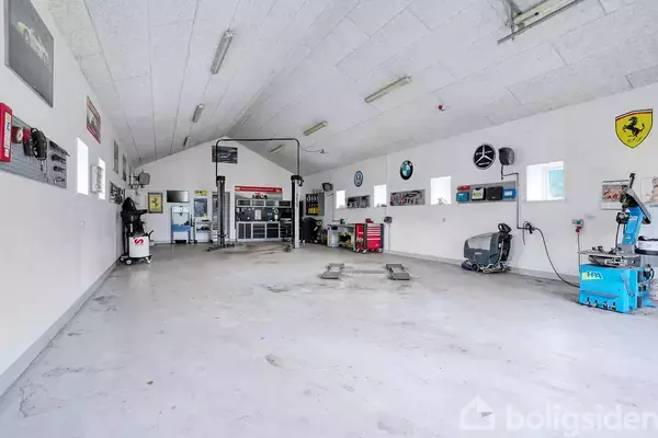 Et garageværksted med en bilhøj, omgivet af værktøj og bildekorationer på væggene. I baggrunden ses forskellige værktøjsstationer og en indgangsdør.