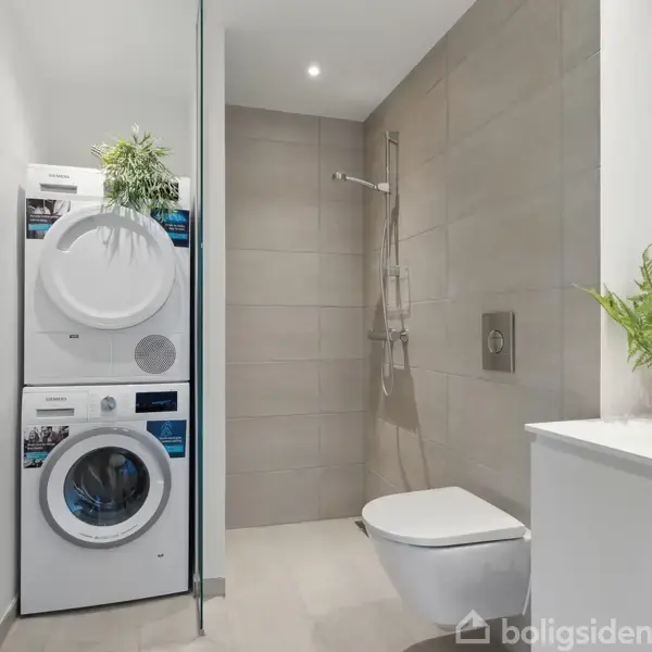 Vaskemaskine og tørretumbler står stablet med en plante ovenpå. De er placeret i et moderne badeværelse med brusekabine, væghængt toilet og hvidt skab med vask og grøn plante.