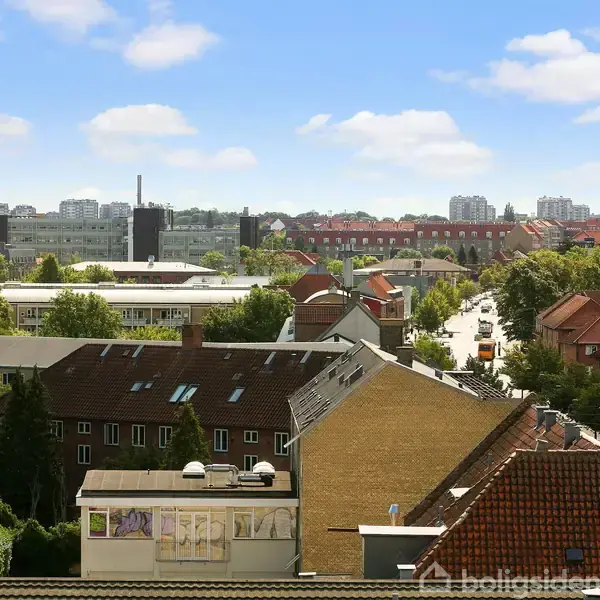 Bygninger står stille i et boligområde med røde tage og grønne træer, mens en solrig himmel danner baggrunden. Bevægelser bemærkes blandt skygger og lys.