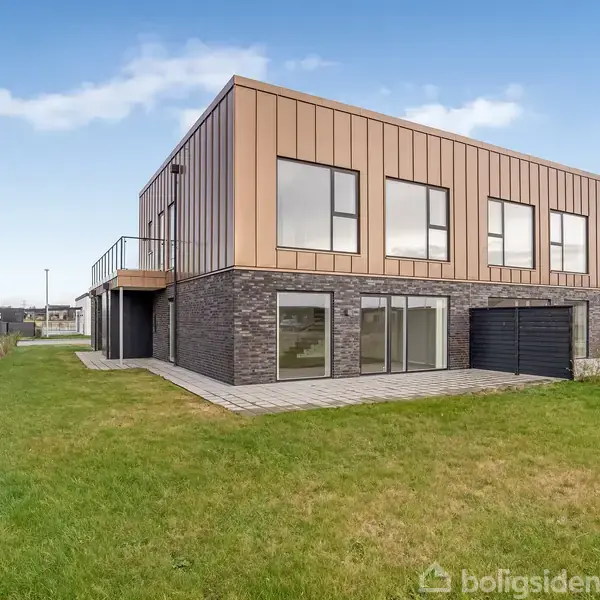 To-etagers moderne hus med fladt tag og store vinduer står på en nyslået græsplæne i et roligt kvarter omgivet af andre lignende boliger.