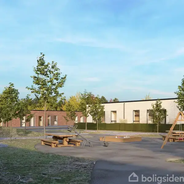 Legeplads med gynger og borde-bænkesæt omgivet af græs og nyplantede træer. Moderne lave bygninger i baggrunden under en klar blå himmel.