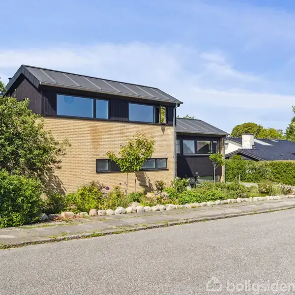 Toetagers hus med fladt tag og store vinduer står ved en vej. Omgivet af træer og buske, ligger det i et villakvarter.