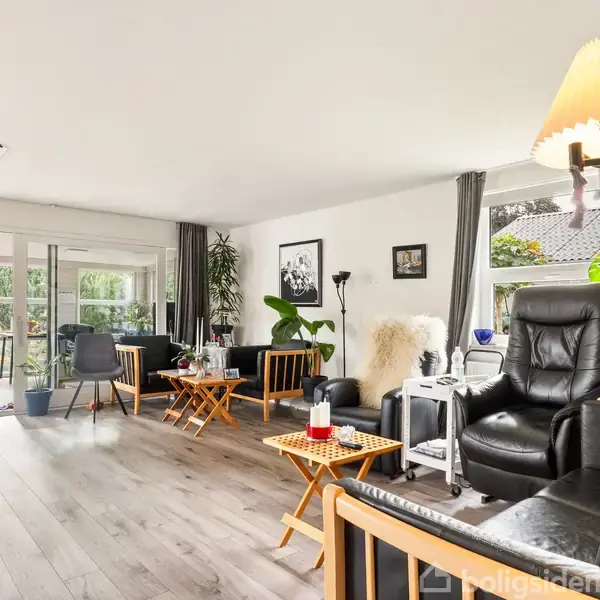 En stue med sorte lædermøbler og træborde, hvor en lampe lyser et rum med åbne glasdøre til en terrasse. Planter og dekorative elementer skaber en indbydende atmosfære.