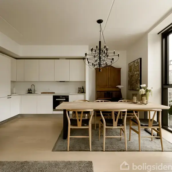 En spisestue med et stort, træbord omgivet af seks stole. En moderne lysekrone hænger over bordet. Køkkenet har hvide skabe, og store vinduer lader naturligt lys ind.