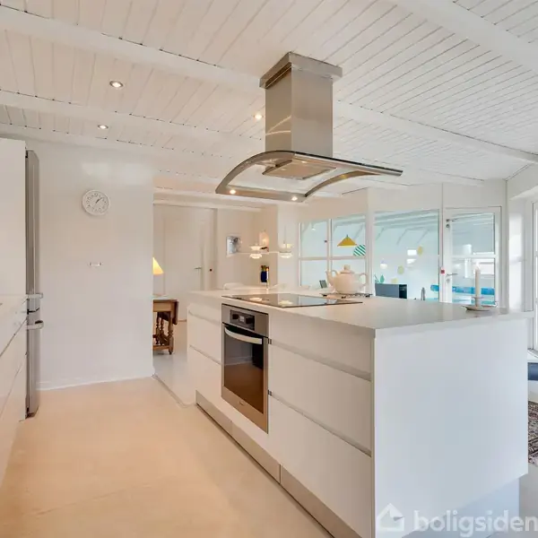 Et moderne køkken med hvidt interiør og en ø i midten. Køkkenet har en glasdør til en terrasse samt en væg med kunst.