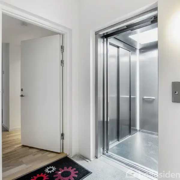 Elevator står åben, klar til at transportere passagerer, i en lys gang med åbne døre og trægulv.