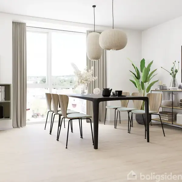 Et spisebord med seks stole står i et lyst rum. Over bordet hænger to lamper. Til højre er en plante og en kommode med dekorationer, mens der er bogreoler til venstre.