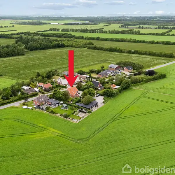 Rødt hus fremhævet med pil står blandt flere bygninger. Handling foregår i en landsby omgivet af grønne marker og skovområder.
