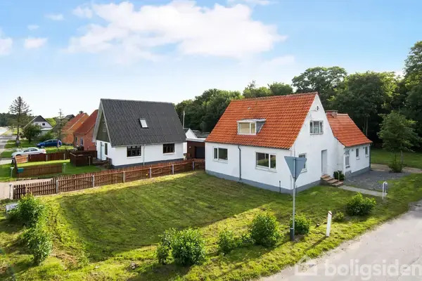 To huse står side om side med nymalede facader og røde eller sorte tegltage. De er omgivet af velplejede græsplæner og træer, beliggende i et roligt villakvarter.