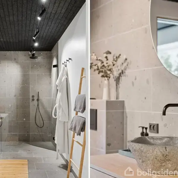 Badeværelse med moderne indretning; brusekabine med regnvandsbruser og beige fliser. Til højre en vask i sten på træbordplade, med rund spejl over, og lys dekoration.