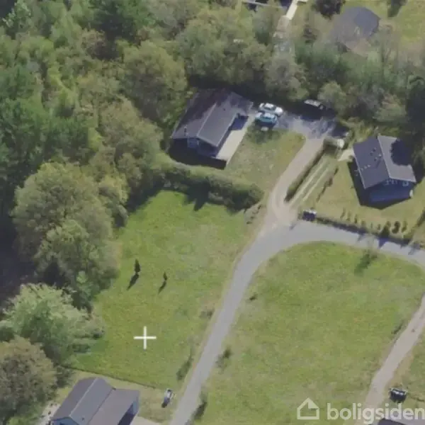 Huse set ovenfra med grønne omgivelser og veje imellem. To huse er tæt på hinanden, omgivet af træer og græsplæner. En hvid bil kan ses parkeret i indkørsel.