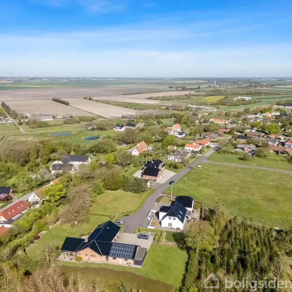 Landskab med spredtliggende huse; flere er omkranset af grønne marker. Solpaneler ses på et tag. En vej løber gennem området, der strækker sig mod horisontens åbne marker.