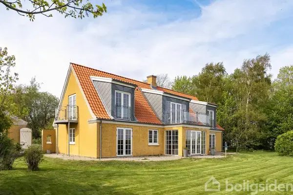 Et gult to-etagers hus med rødt tegltag står roligt i en grøn have. Store vinduer og altaner giver et lyst udtryk. Baggrunden omfatter træer og en blå himmel.