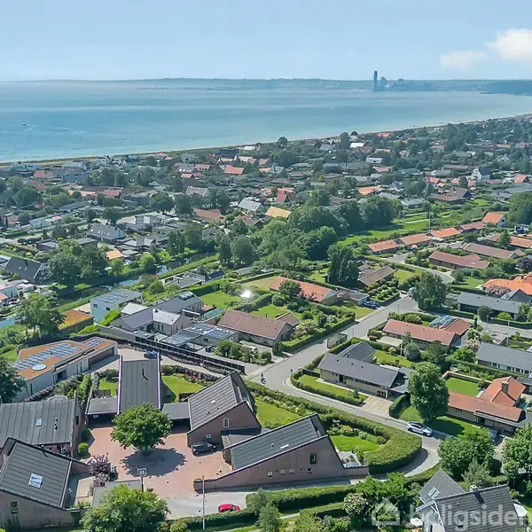 Et boligområde med huse spredt ud over et frodigt landskab. Huse ligger tæt ved kysten, hvor havet kan ses i baggrunden med en bred horisont.