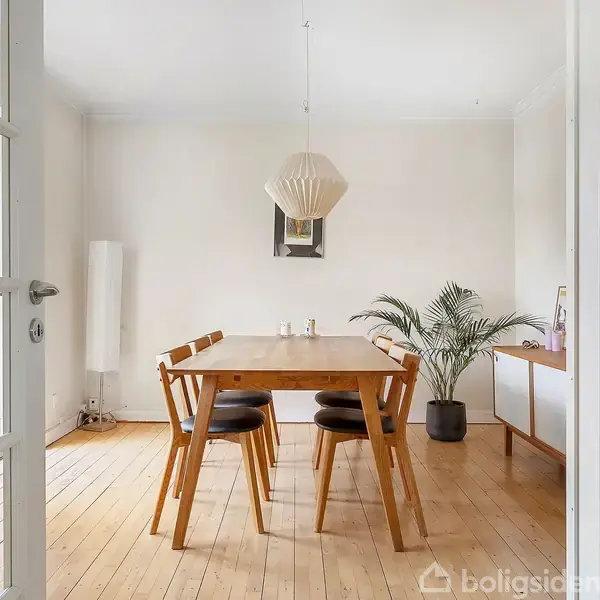 En træspisebord med fire stole står i et lyst rum. En moderne lampe hænger over bordet. Der er en plante i en potte ved siden af et lille konsolbord.