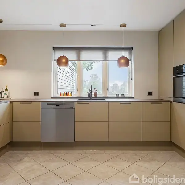 Køkken med beige skabe, tre hængende kobberlamper, opvaskemaskine, ovn, og stort vindue med udsigt. Rummeligt og moderne design med gulvfliser og træpaneler. Flasker og glas er placeret nær vinduet.