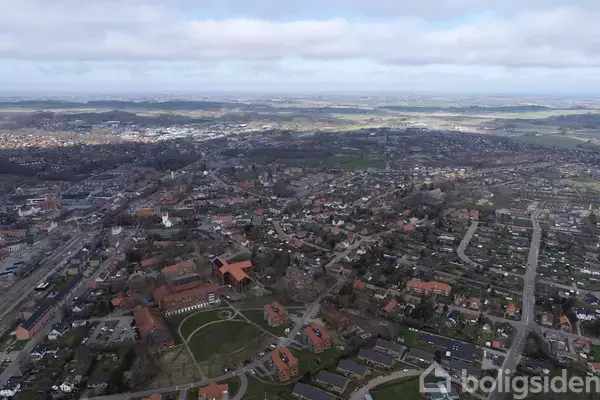 Byområde set ovenfra med huse og veje, spredt over en dal og bakket landskab. Der er skyer på himlen i baggrunden.