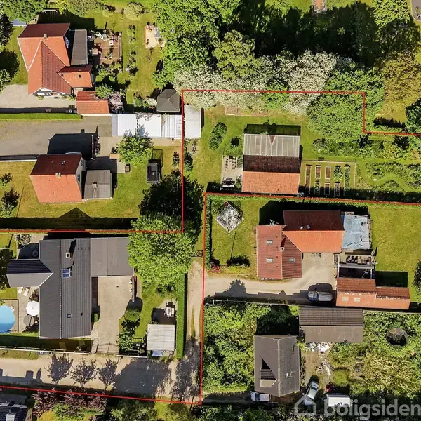 Luftfoto over kvarter med flere enfamiliehuse, haver og træer, omkranset af veje. En rød linje markerer en særlig grund med et større grønt område og haveanlæg.
