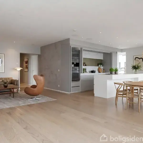 Stue og køkken i åbent rum. To lænestole står ved et lille sofabord. Spisebord med stole og en dekorativ lampe. Moderne køkken med hvide overflader og integrerede apparater.