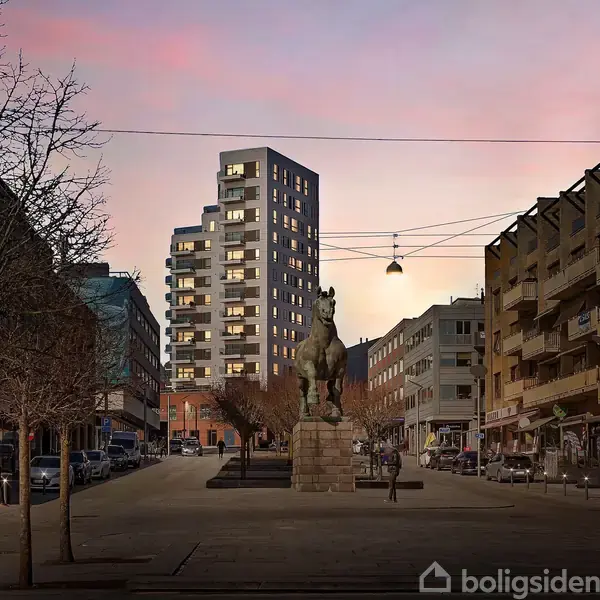 En statue af en hest står stille på en sokkel i en bymidte. Omgivet af moderne bygninger og gadelamper under en skumringshimmel med lyserøde nuancer.