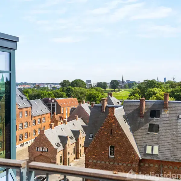 Glasbygning står stille med udsigt til række af historiske murstenshuse. I baggrunden strækker grønne trækroner sig mod himlen under en blå himmel.